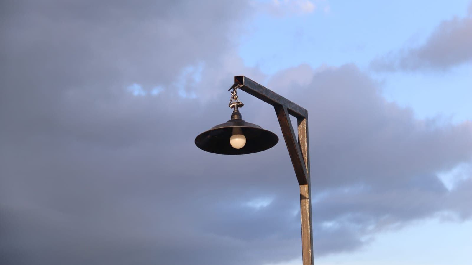 A shepherd's hook standing on a lawn against an open sky